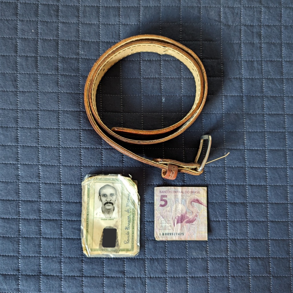Cinto marrom de couro, carteira de identidade e uma nota de 5 reais, colocadas em cima de um fundo azul escuro